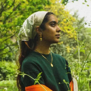 Nikhita Vakkalagadda, 30 under 30 nominee in 2023 smiling and looking off camera with flowers and trees around her.