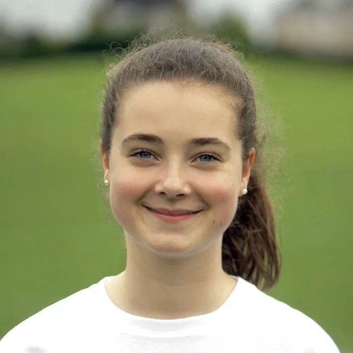 Abby Lang smiling at the camera, wearing a white t-shirt with brown hair pulled into a ponytail