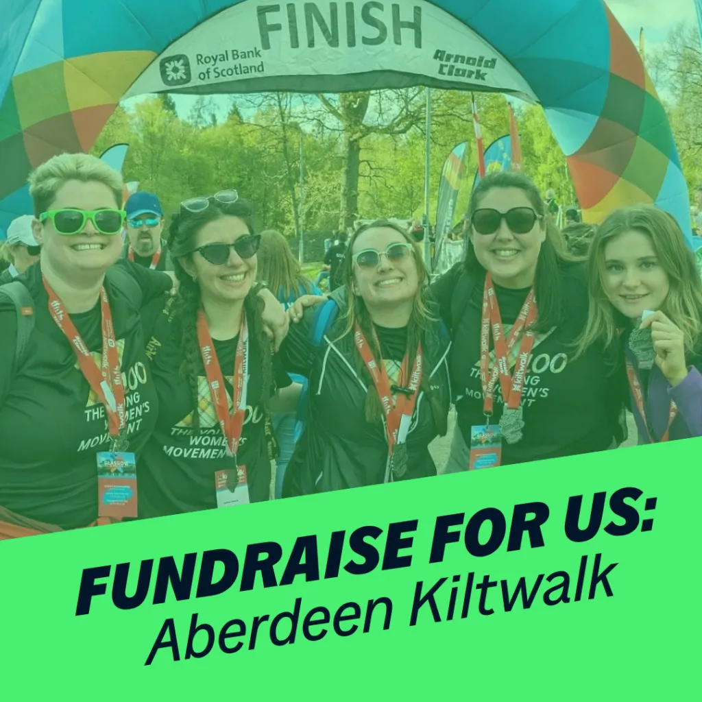 Five women smile at the camera. behind them is the kiltwalk finish line. Green banner reads 