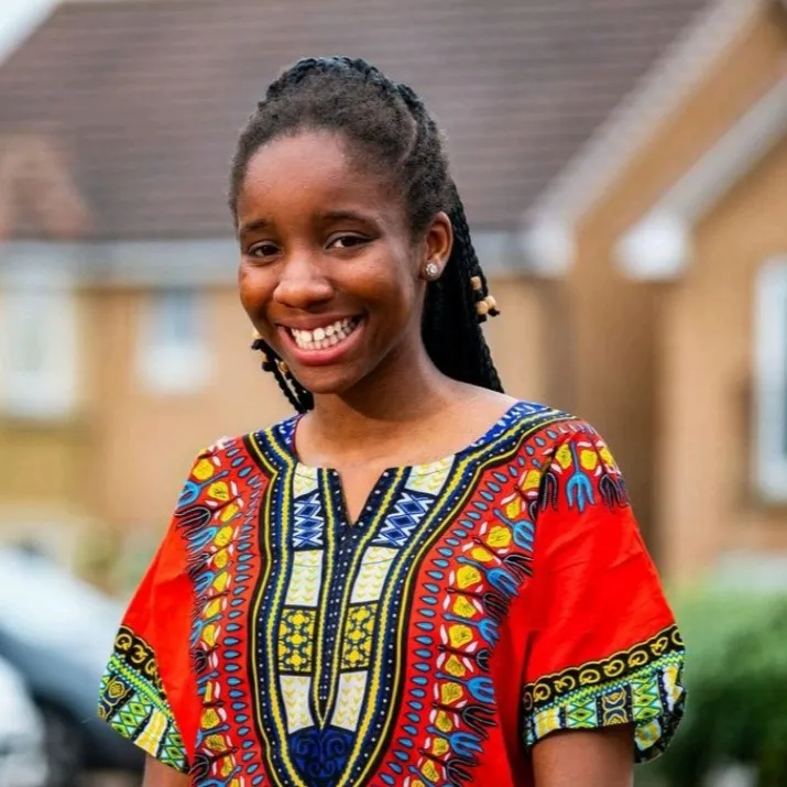 Amanda Amaeshi smiling at the camera, standing on a street with houses behind