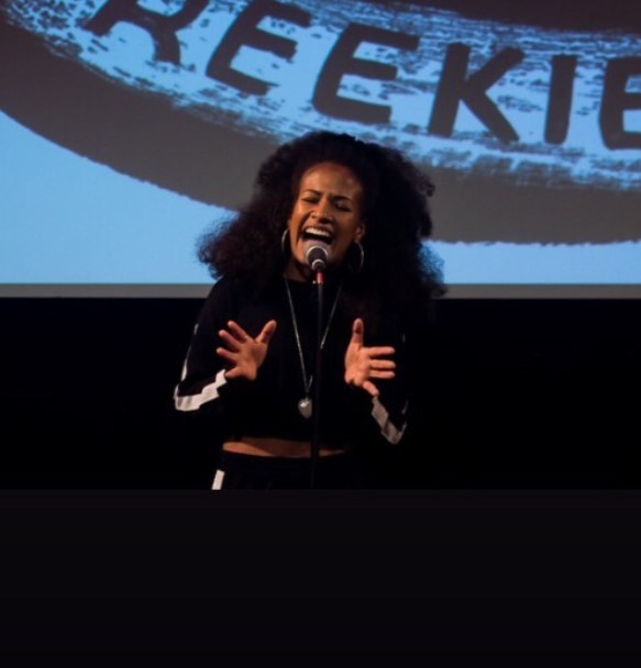 Courtney Stoddart performing on stage, speaking emphatically into a microphone on a mic stand