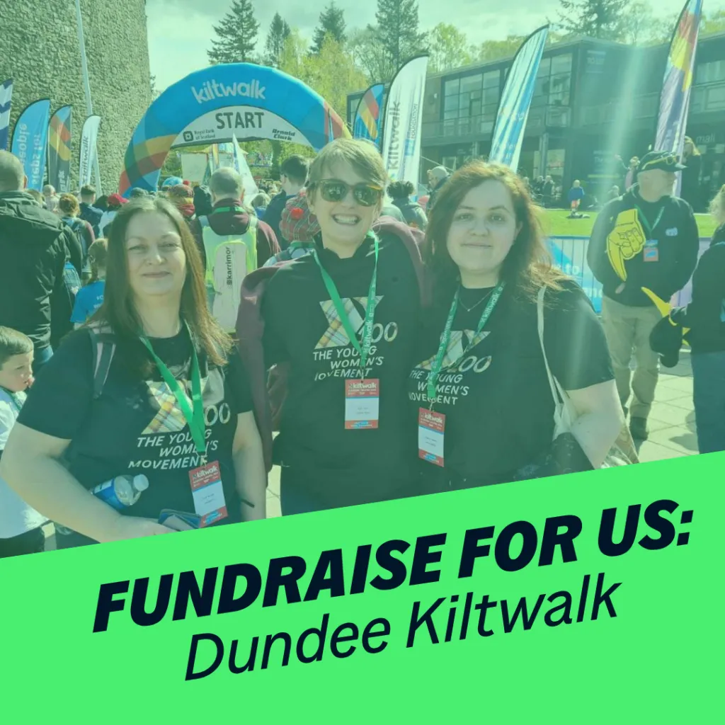 Three women smile at the camera. Behind them is the kiltwalk finish line. Green banner reads 