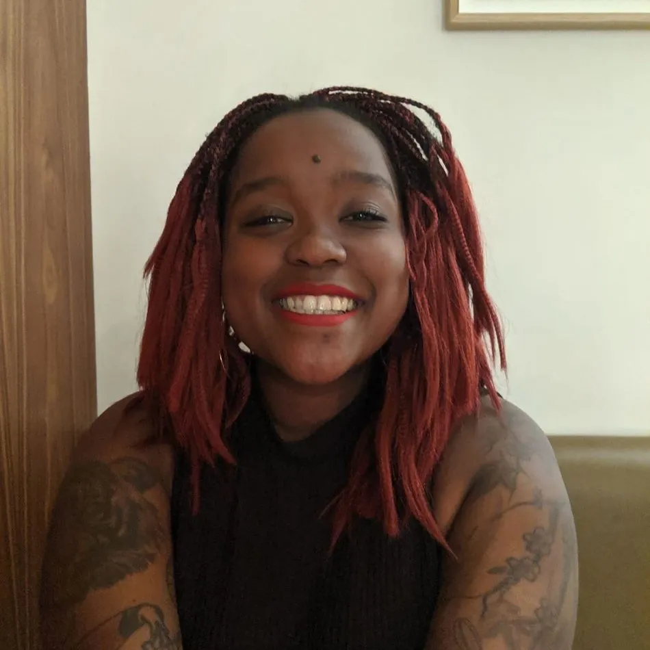 Lizzie Riungu smiling at the camera, with arm tattoos visible and pink hair