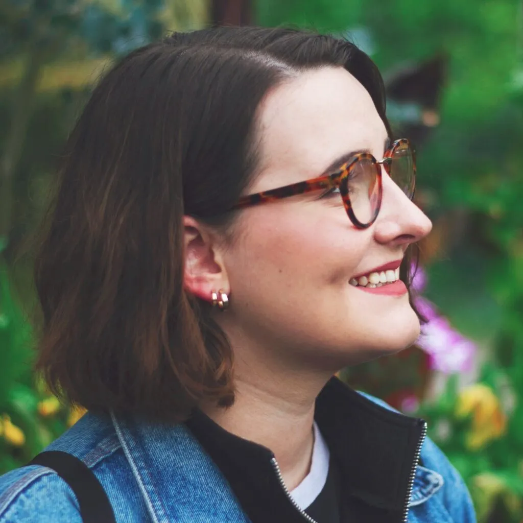 Mel Reeve smiling off camera in profile view, with flowers visible behind her