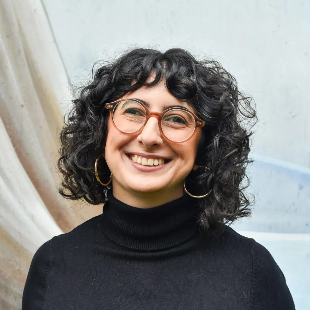 A photo of Samar, who has dark curly hair and glasses and is smiling at the camera.