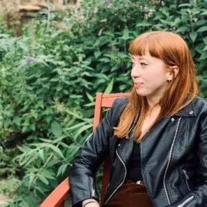 Tor Scott looking off camera in profile view, with a tall hedge behind her