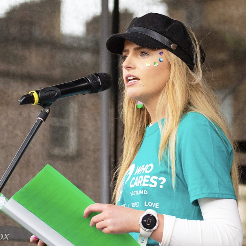 Eireann giving a speech into a microphone whilst holding a green folder.