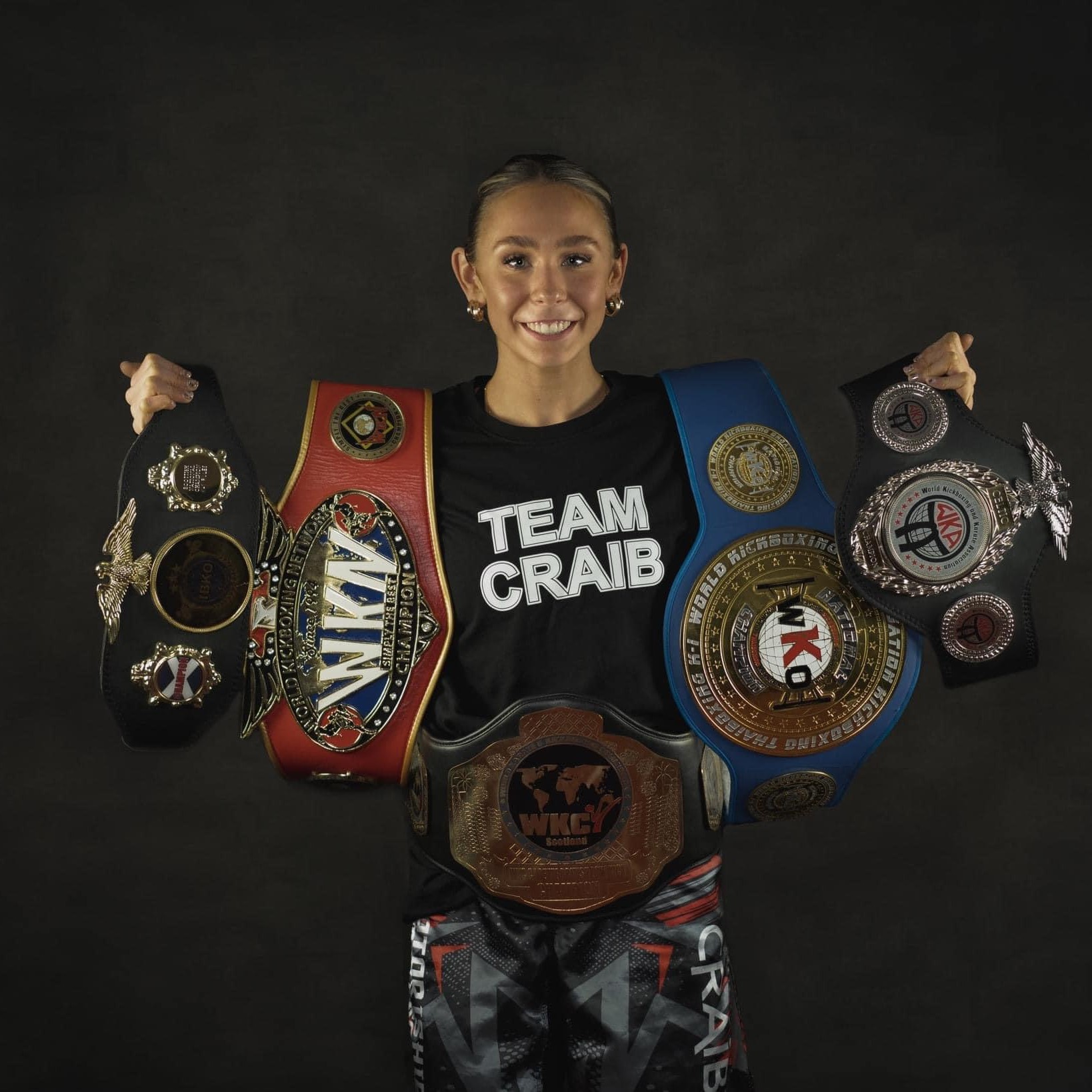 Eilidh smiling at the camera holding 4 winning belts.