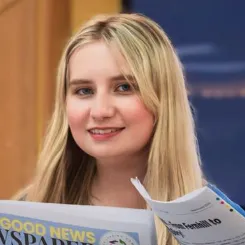 Emma smiling at the camera holding a newspaper.