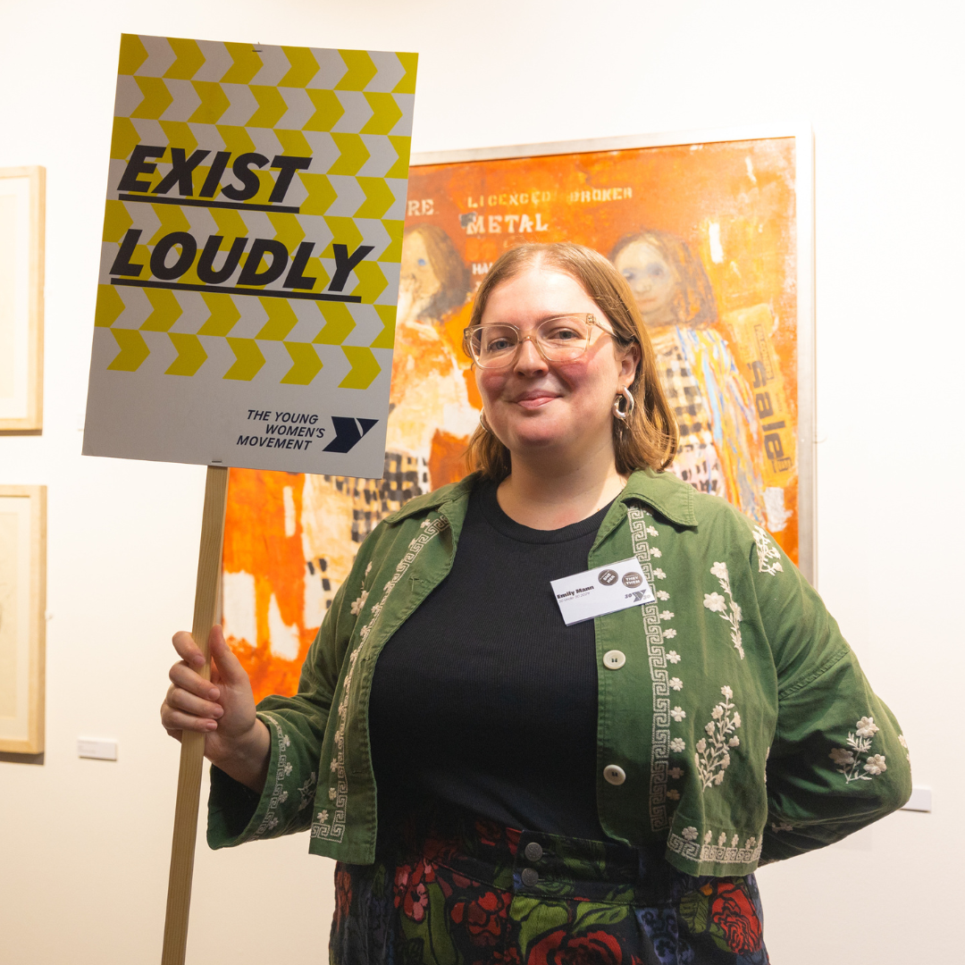 Emily Mann at 30U30 event, holding a placard that says Exist Loudly