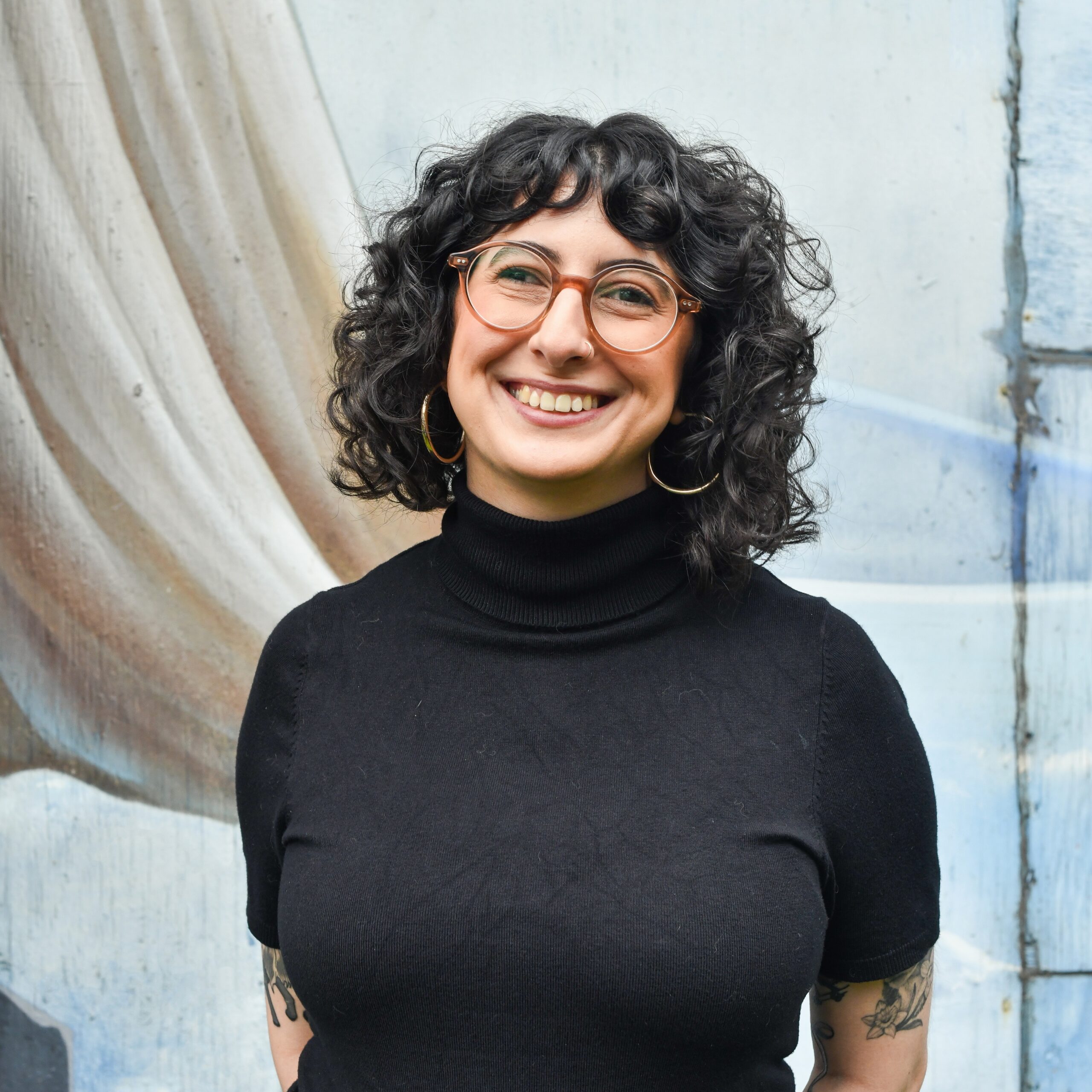 Photo of Samar with dark curly hair and glasses, smiling at the camera.