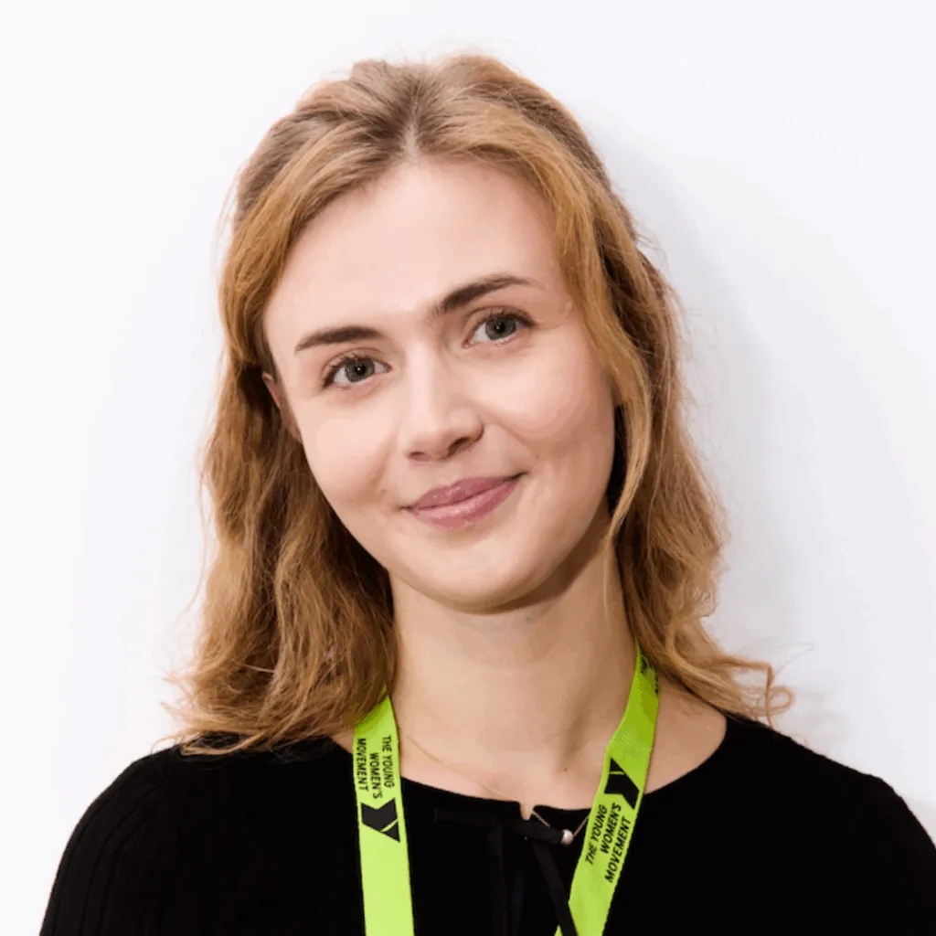 Robyn smiling with a white wall behind, wearing a Young Women's Movement lanyard