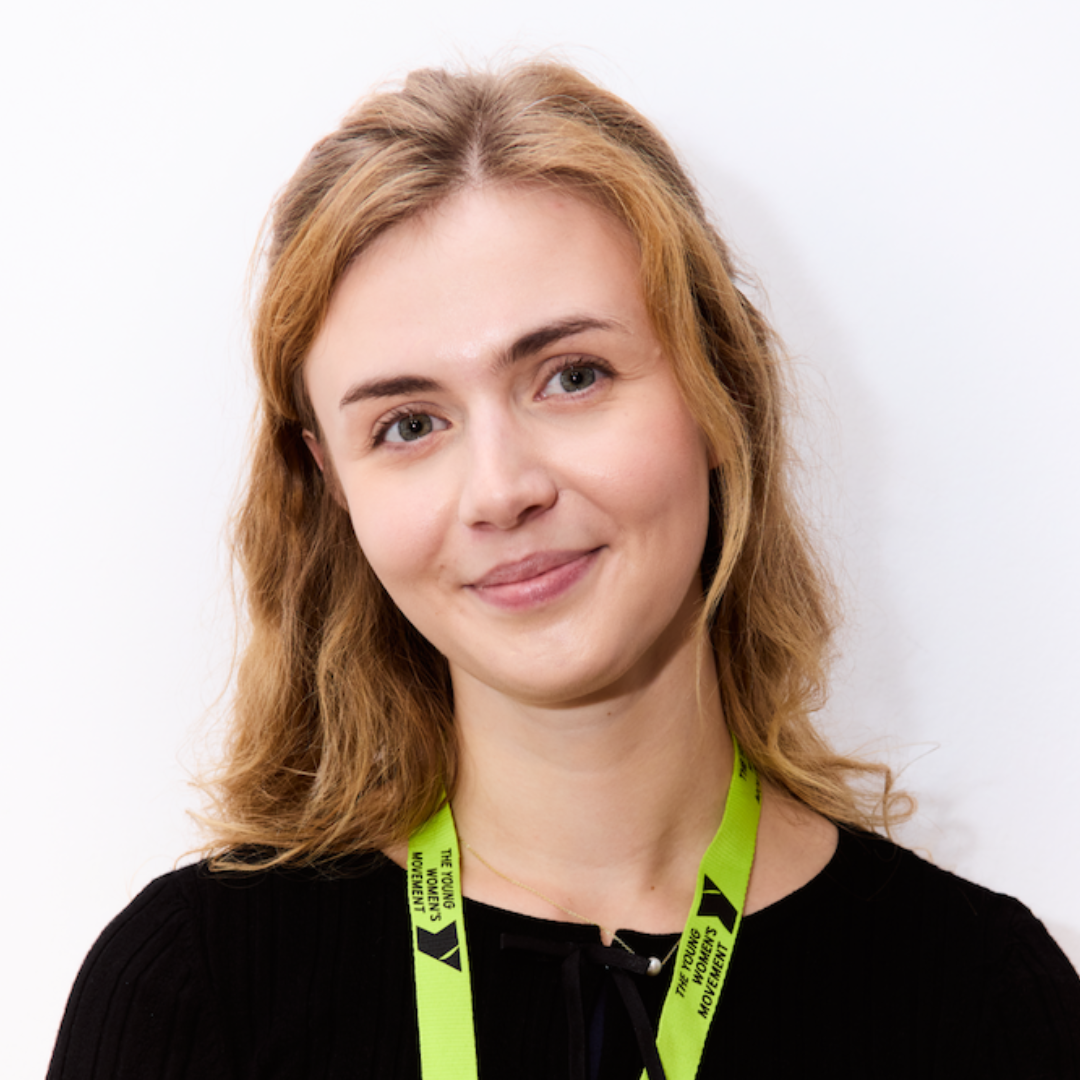 Robyn smiling with a white wall behind, wearing a Young Women's Movement lanyard