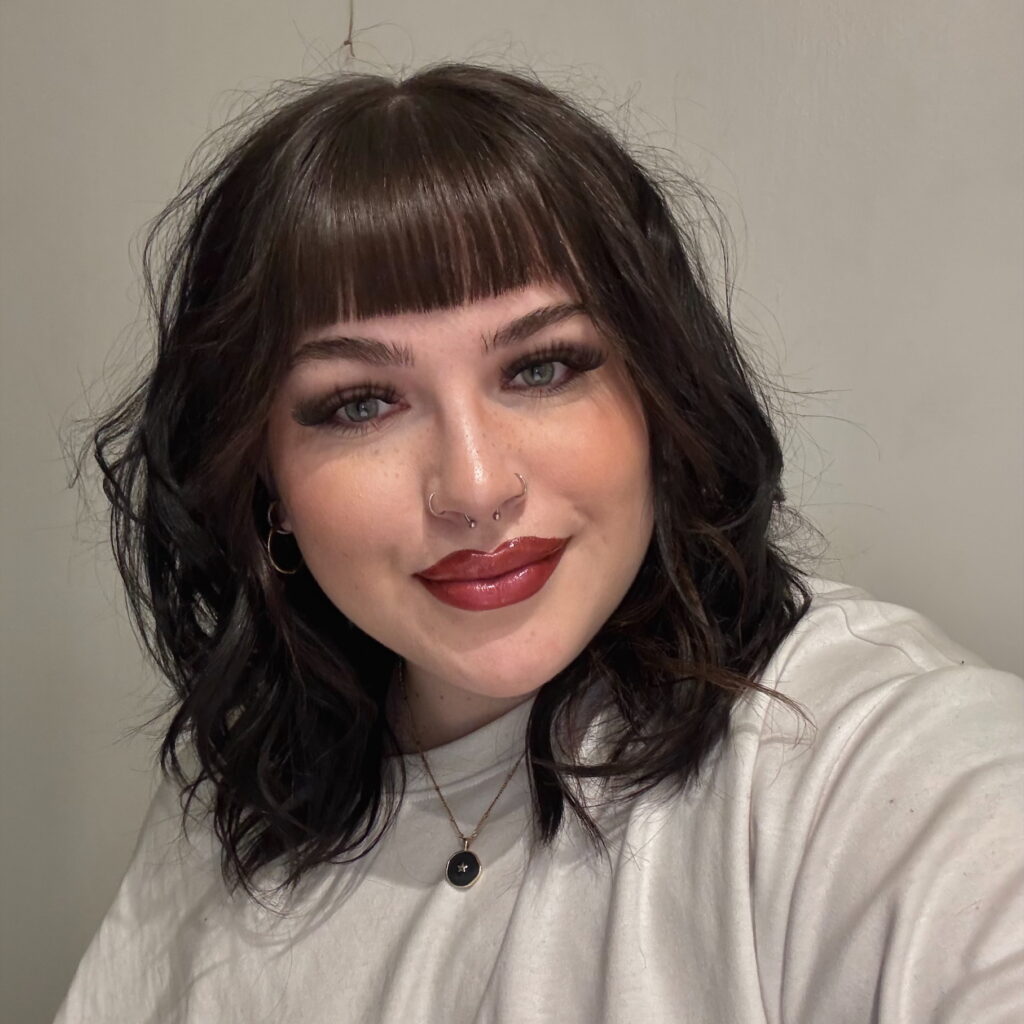 Beth has dark hair with a fringe, and pale skin.