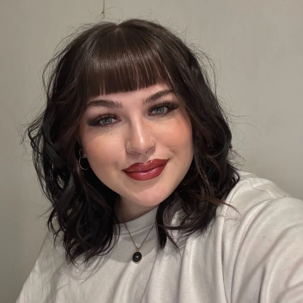 Beth has dark hair with a fringe, and pale skin.