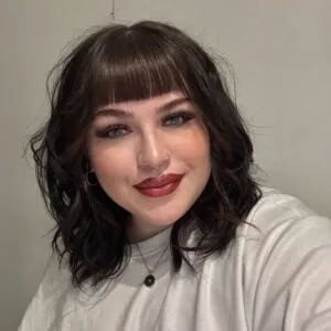 Beth has dark hair with a fringe, and pale skin.