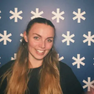 Chloe has long blonde hair and pale skin. She is standing in front of a blue background with stars on it.