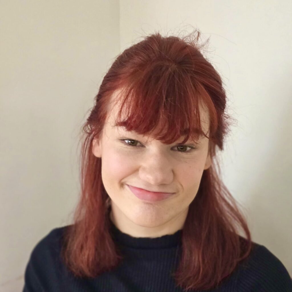 Melissa has pale skin and red hair with a fringe.