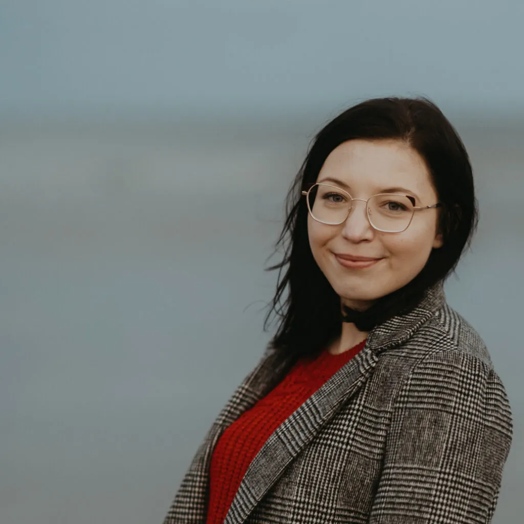 Niocola has dark hair and pale skin. She is wearing a checked jacket.