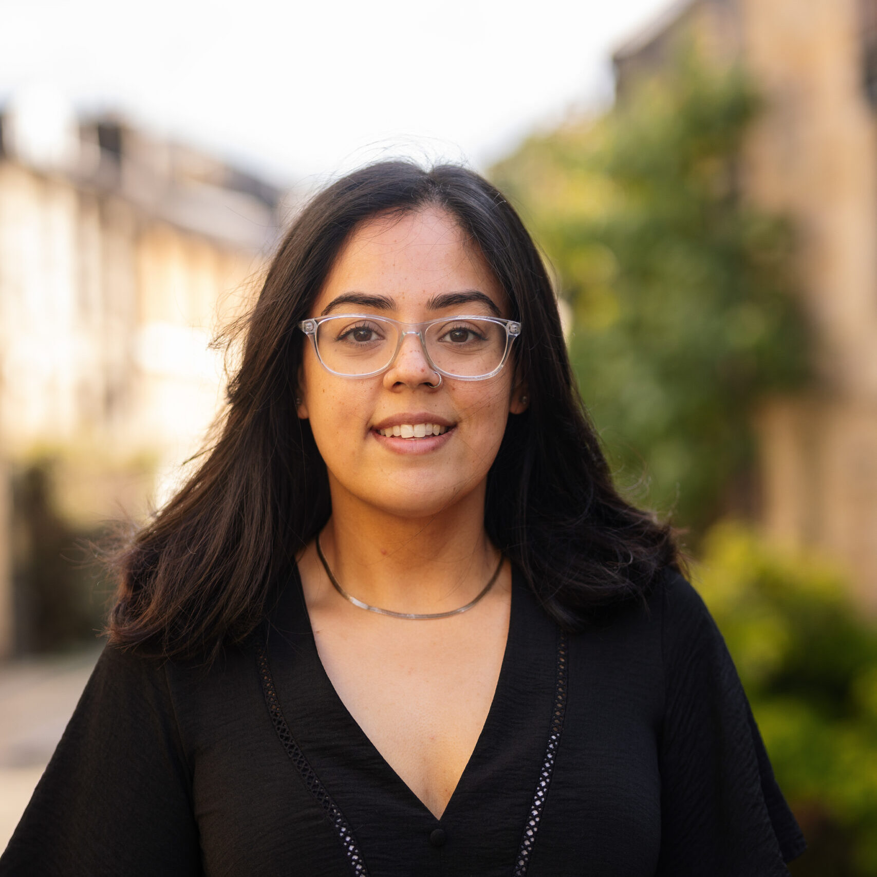 Sidrah has brown skin, long dark hair, and is wearing glasses.