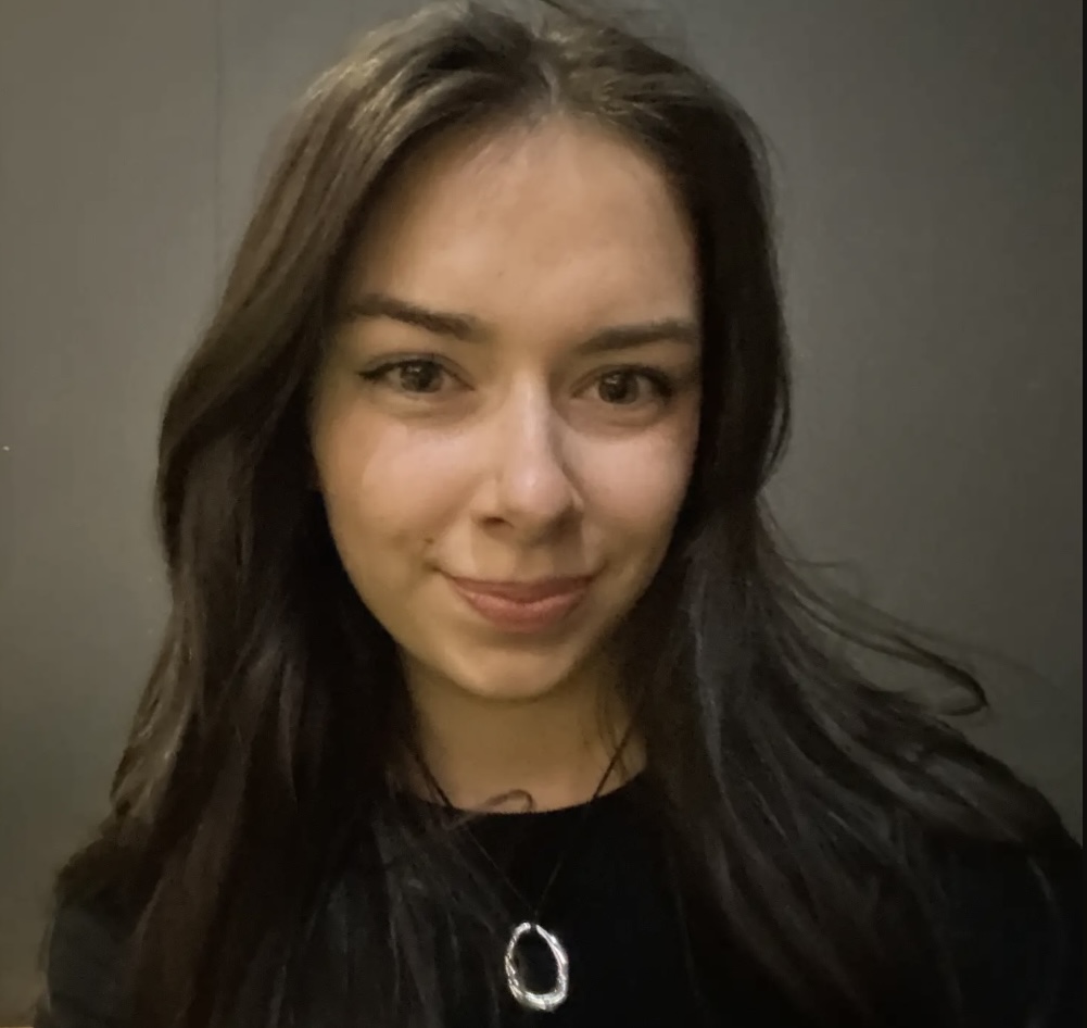 Holly has dark hair and pale skin. She is smiling at the camera.