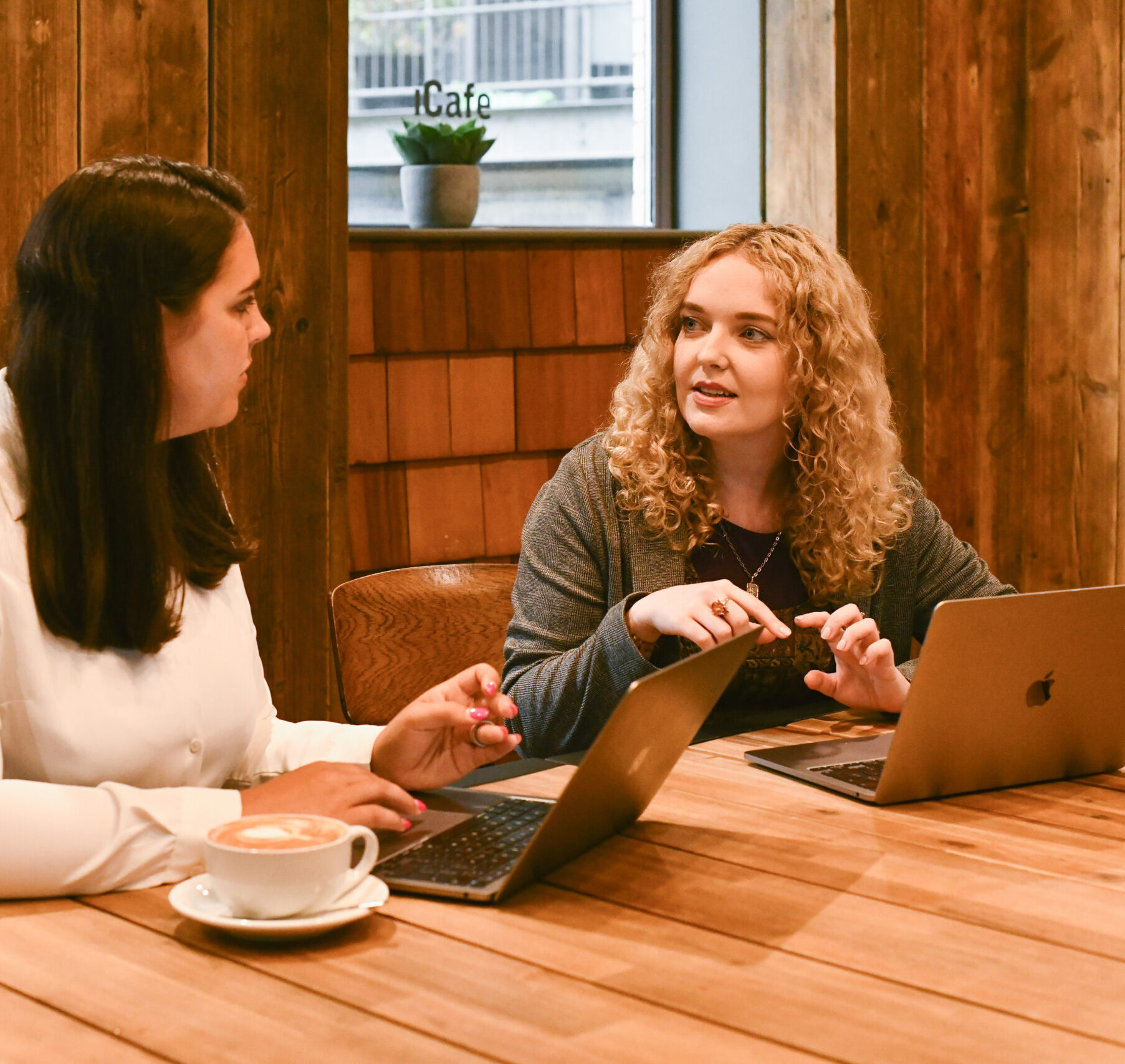 Two women sat at a table with laptops in front of them