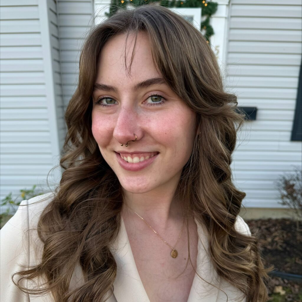 Elizabeth has pale skin and brown hair. She is smiling at the camera.