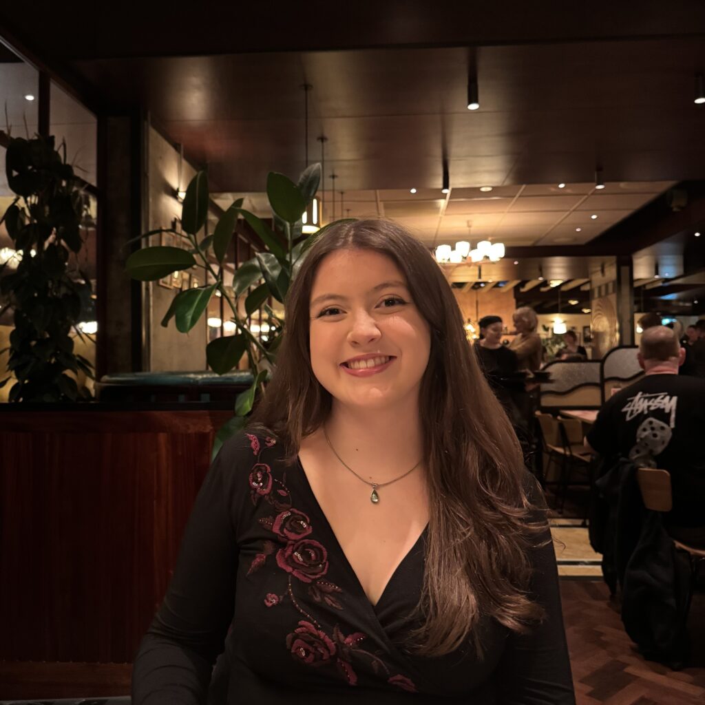 Iona has pale skin and long dark hair. She is sitting in a restaurant.